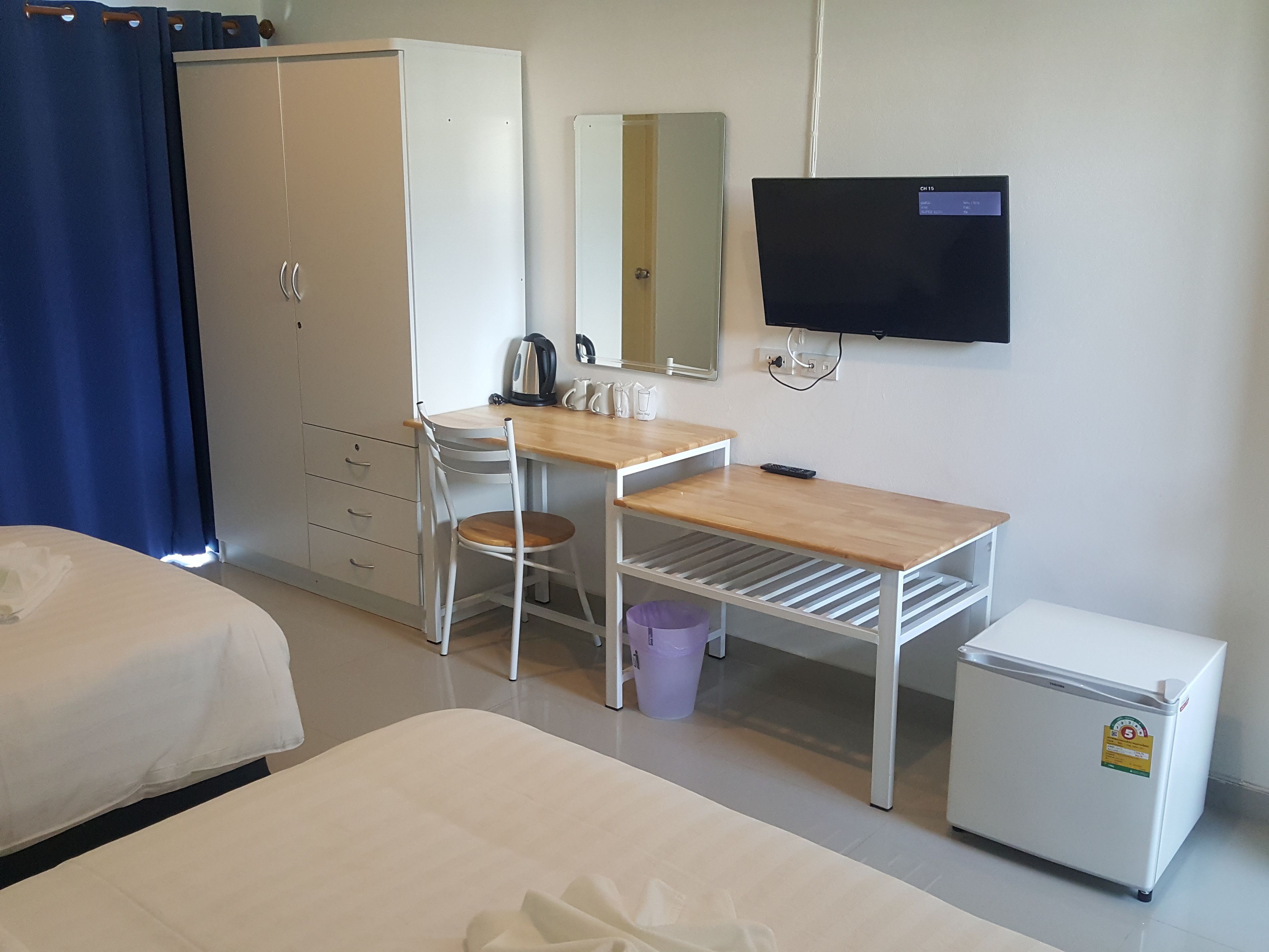 Een hotelkamer met een bed, een bureau met stoel, een kleine koelkast, een televisie en een kledingkast.