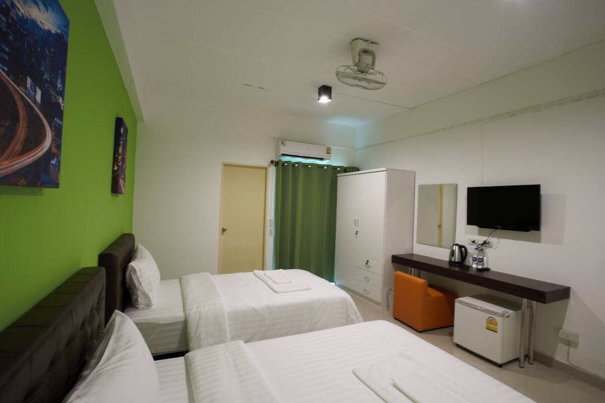A hotel room with two beds, a desk with a television, a mini-fridge, and a green curtain.