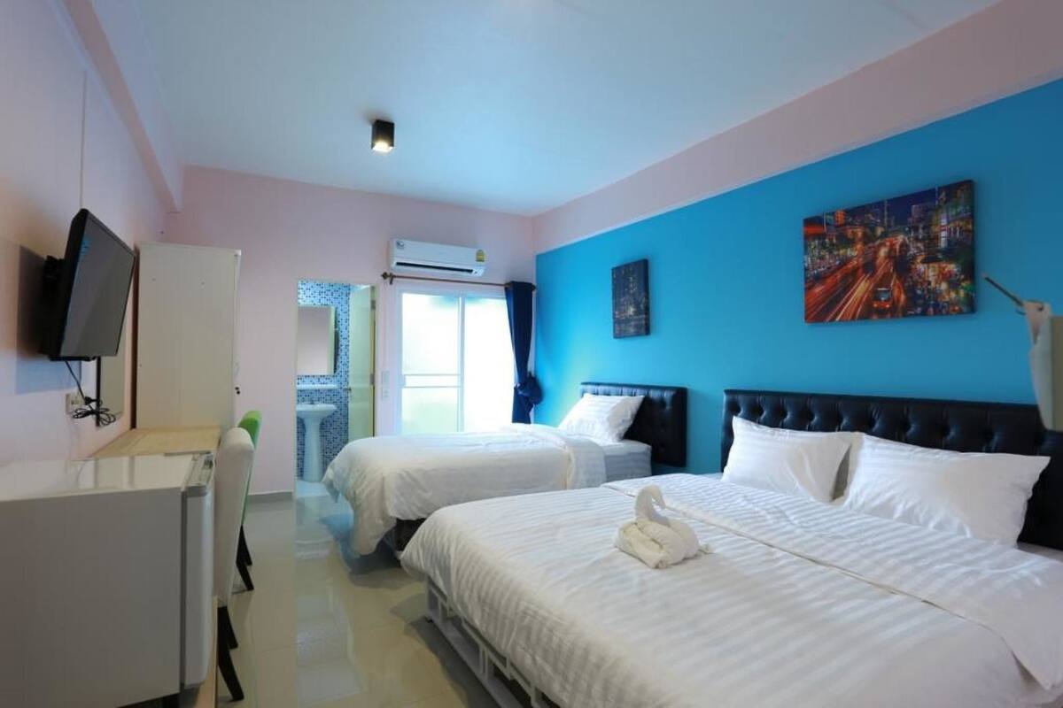 A hotel room with two beds, a TV, a desk, and a window with curtains.