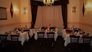 A formal dining room with multiple tables set for service, a chandelier, and wall-mounted lighting. - The Woodland Hotel (Blackpool)