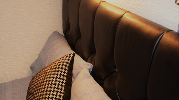 A bed with a brown upholstered headboard, a patterned pillow, and a light-colored bedspread. - The Woodland Hotel (Blackpool)
