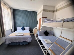 A hotel room with two beds, a window with curtains, a bedside table, and a bunk bed. - The Woodland Hotel (Blackpool)