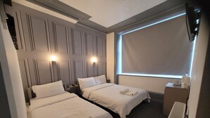 A hotel room with two beds, a large window, and a built-in heater. - The Woodland Hotel (Blackpool)
