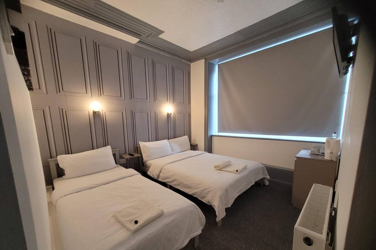 Une chambre d’hôtel avec deux lits, une grande fenêtre et un radiateur intégré.