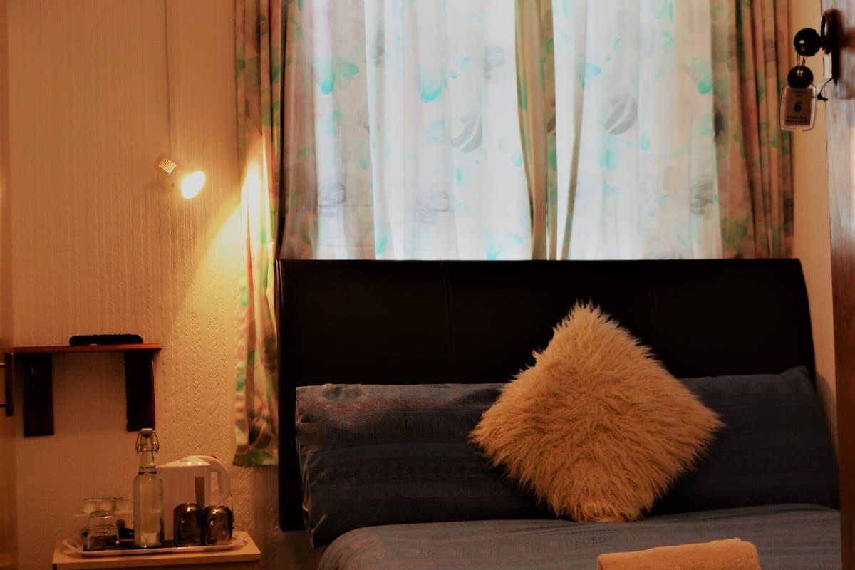 Une chambre à coucher avec un lit, une table de chevet, une lampe et une fenêtre avec des rideaux.
