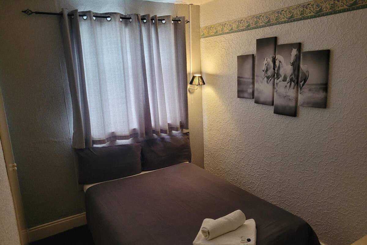 Une chambre d’hôtel avec un lit, un rideau, une lampe fixée au mur et trois tableaux encadrés.