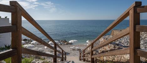 Un escalier en bois qui descend vers une plage, offrant une vue dégagée sur la mer.
