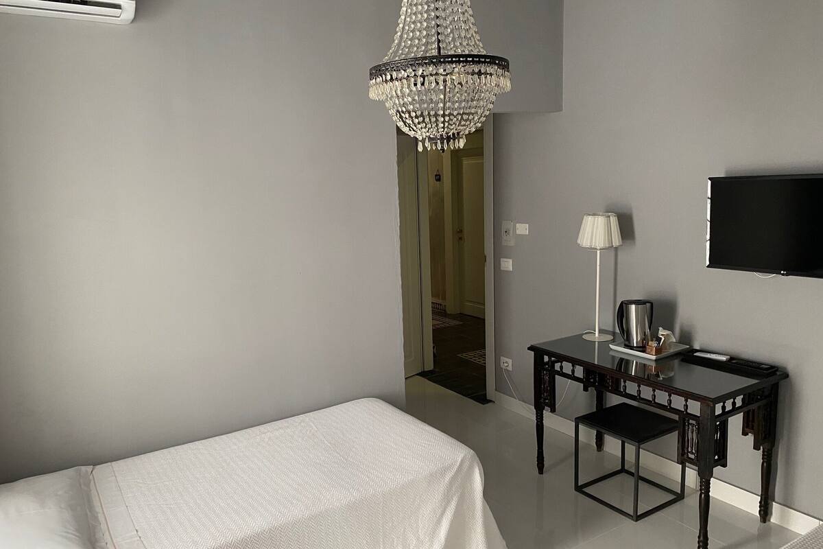 Ein Hotelzimmer mit einem Bett, einem Schreibtisch mit Lampe, einem Fernseher und einer Kristallleuchter.