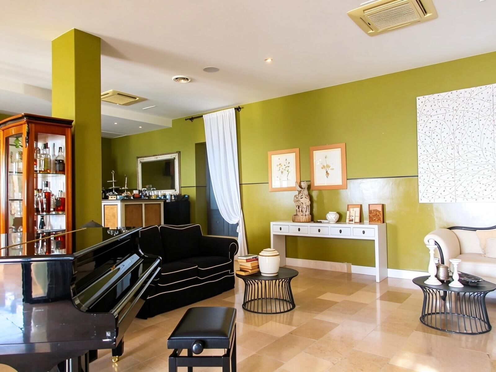 A living room with a piano, a sofa, a coffee table, and a console table with framed pictures.