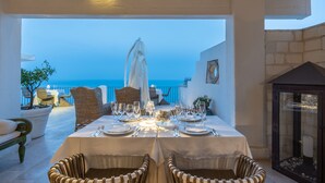 A dining table set for two with a view of the sea, wicker chairs, and a glass cabinet. - La Locanda del Carrubo (Mattinata)