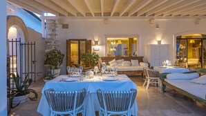 A dining area with a table set for four, surrounded by white wicker chairs, in a room with a high ceiling and stone walls. - La Locanda del Carrubo (Mattinata)