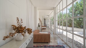 A long, narrow hallway with large windows, a wooden bench, and a white console table with vases. - La Locanda del Carrubo (Mattinata)