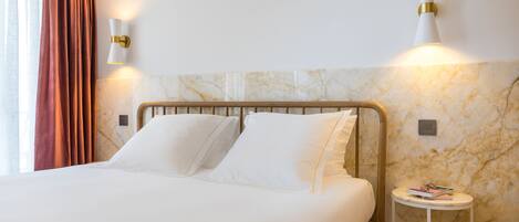 A neatly made bed with white linens, a marble-patterned wall, and a bedside table with a book.