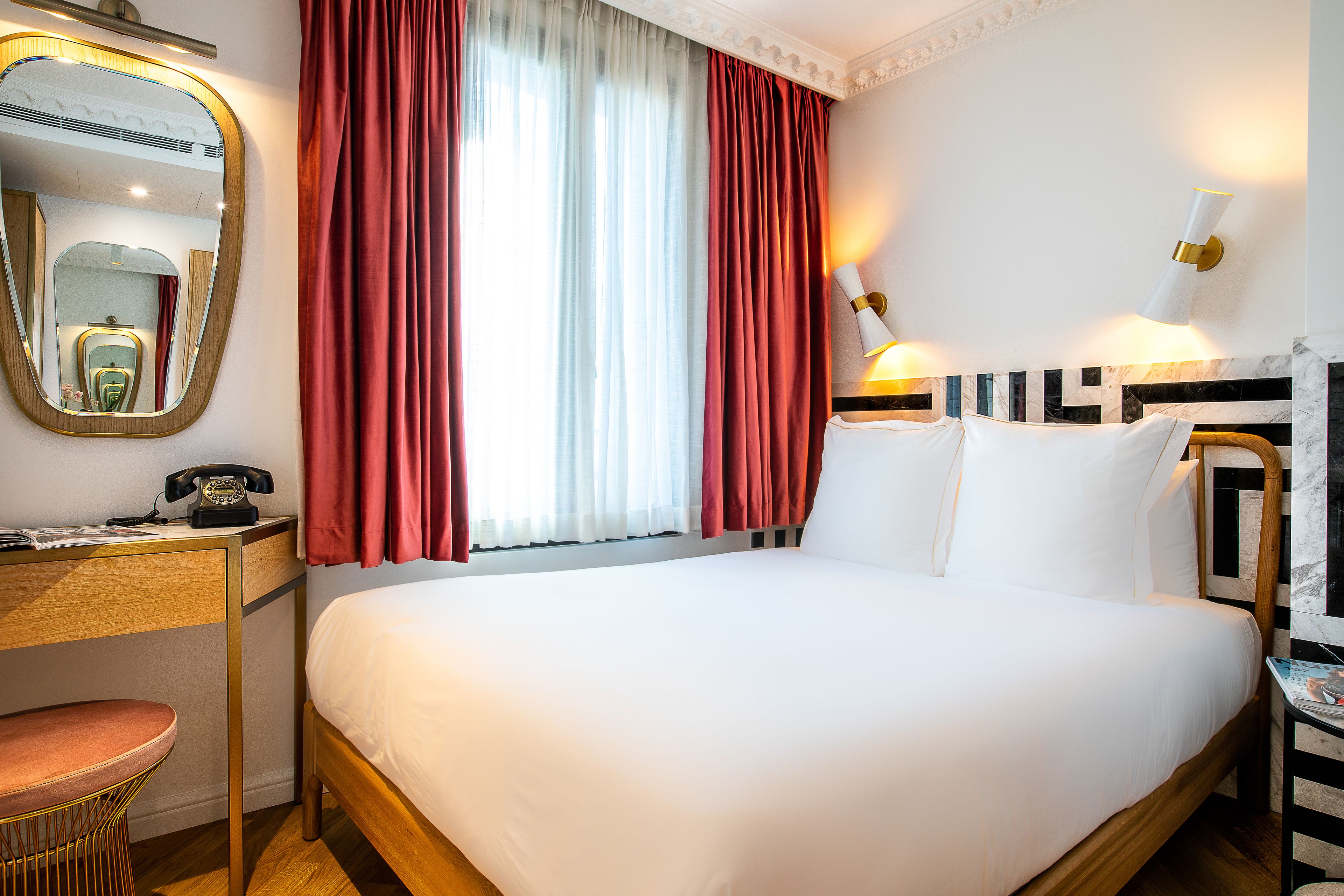 Habitación de hotel con una cama grande, un escritorio con teléfono, una silla, un espejo y una lámpara de pared.