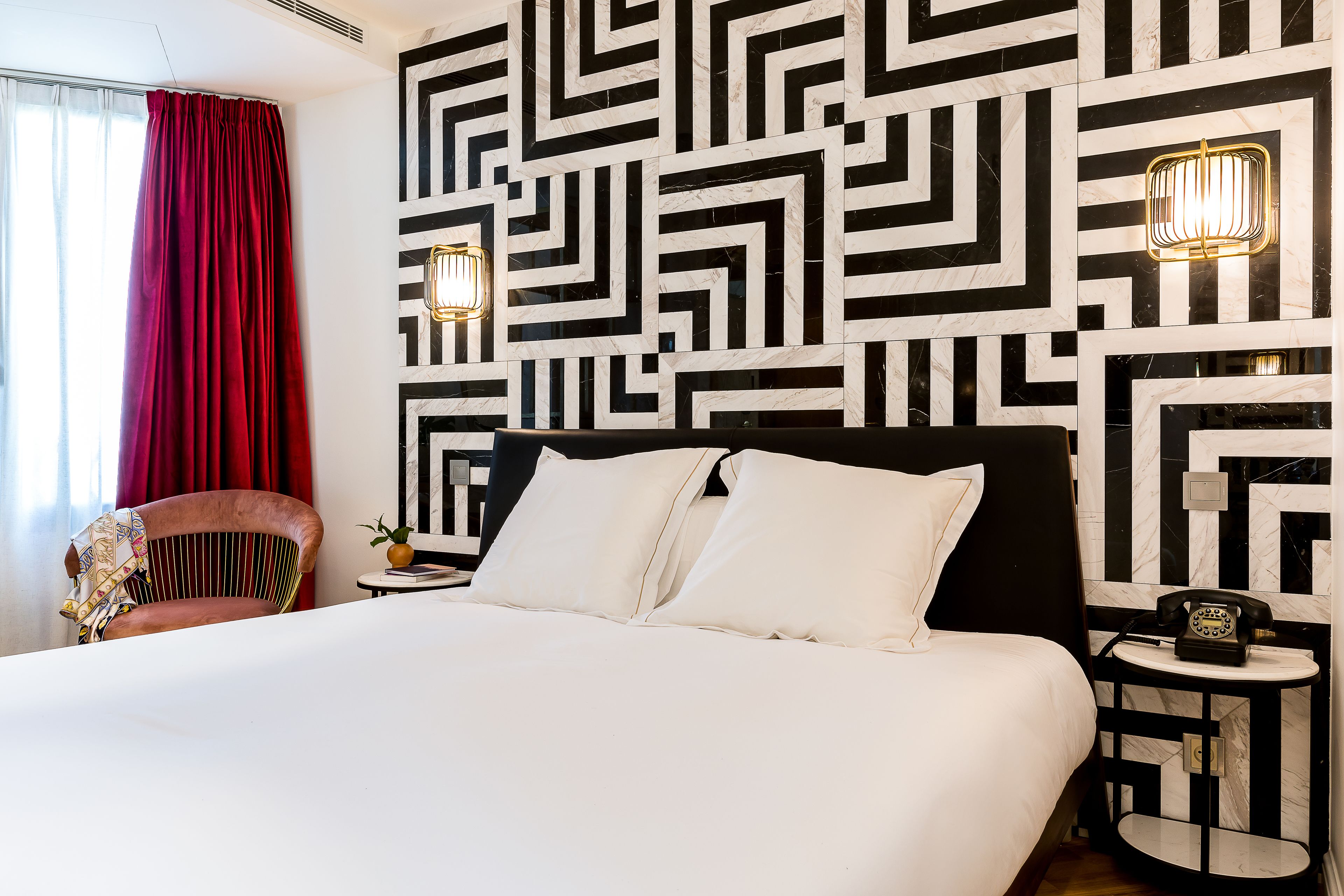 A hotel room with a large bed, a red curtain, a patterned wall, and two bedside lamps.
