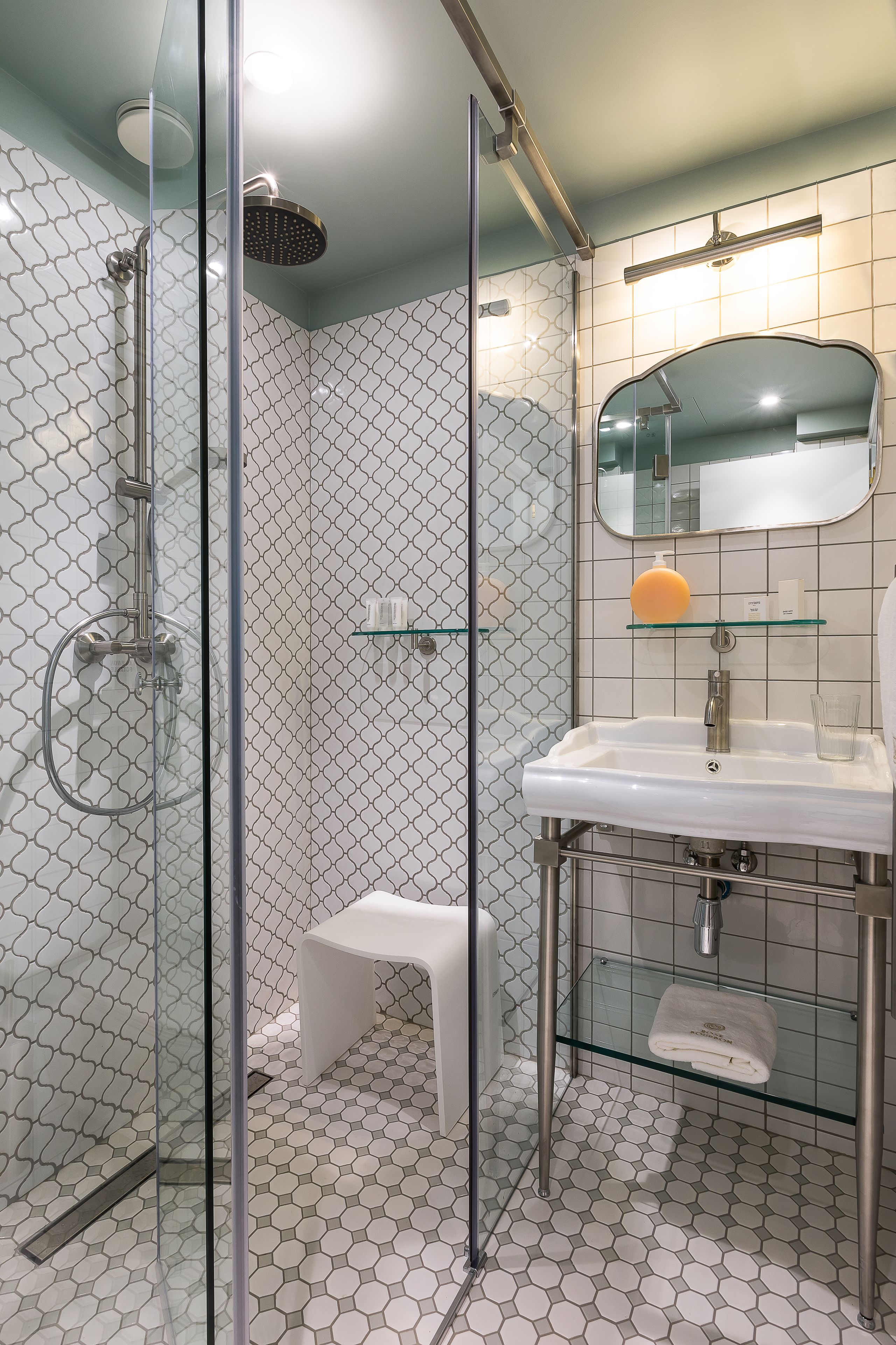 Une salle de bain moderne avec une douche à parois de verre, un lavabo blanc et un petit tabouret.