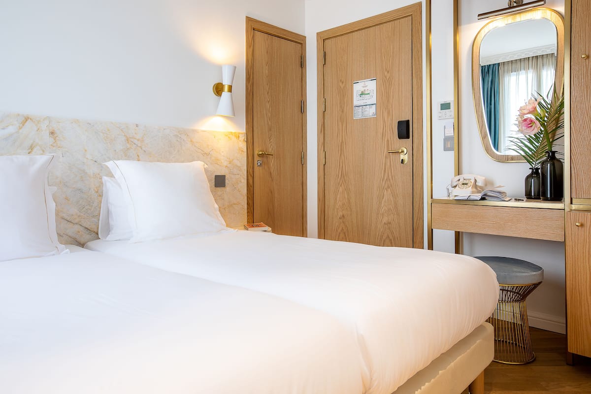Habitación de hotel con cama, armario de madera, mesita de noche con lámpara y espejo con arreglo floral.