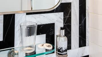 Casa de banho com um espelho grande, azulejos de mármore a preto e branco, uma prateleira de vidro com artigos de higiene pessoal e um jarro de vidro.