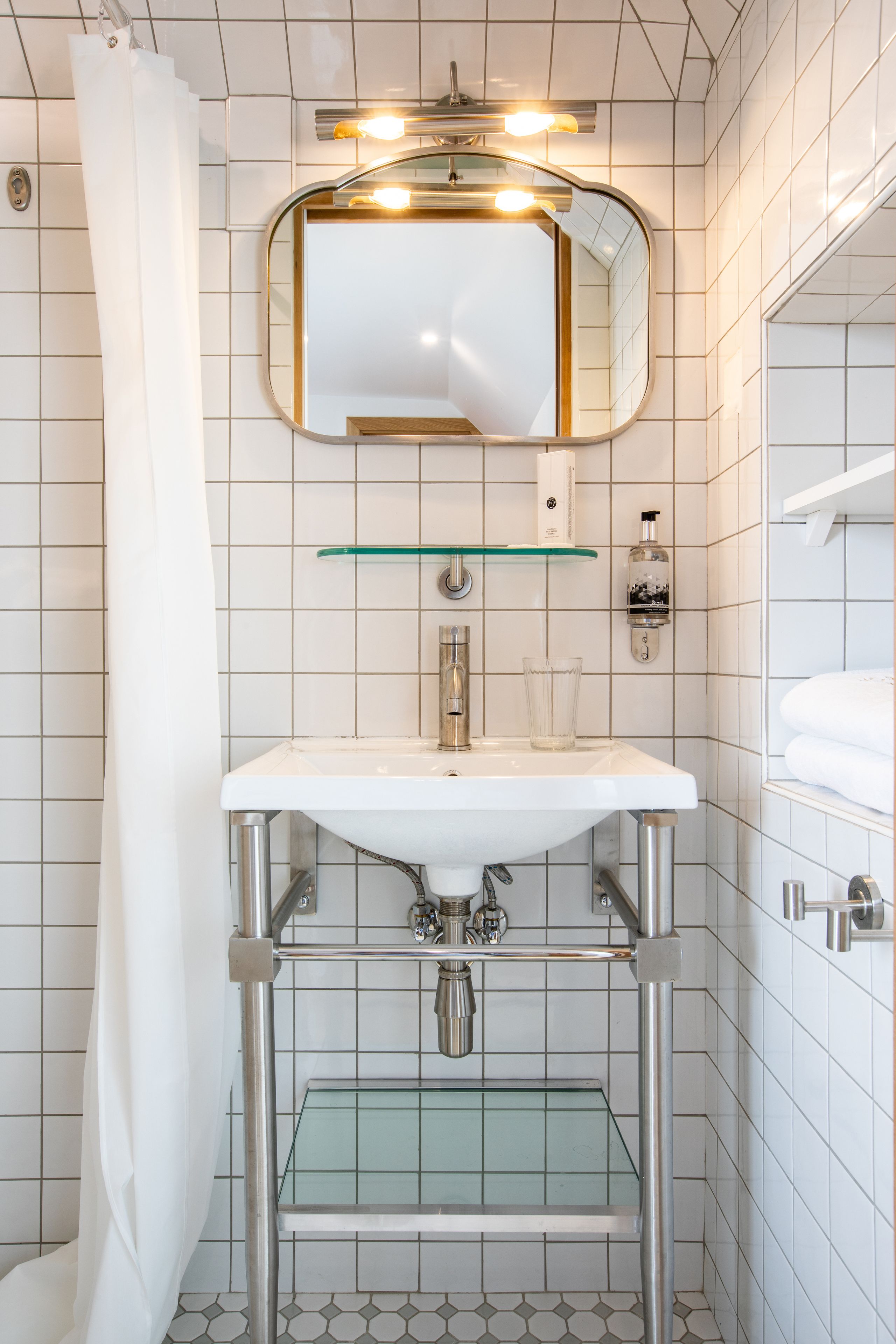 Un baño con un lavabo blanco, un estante de vidrio encima, un espejo y una cortina de ducha.