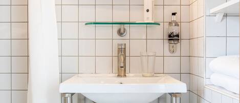 Un baño con un lavabo blanco, un estante de vidrio encima, un espejo y una cortina de ducha.