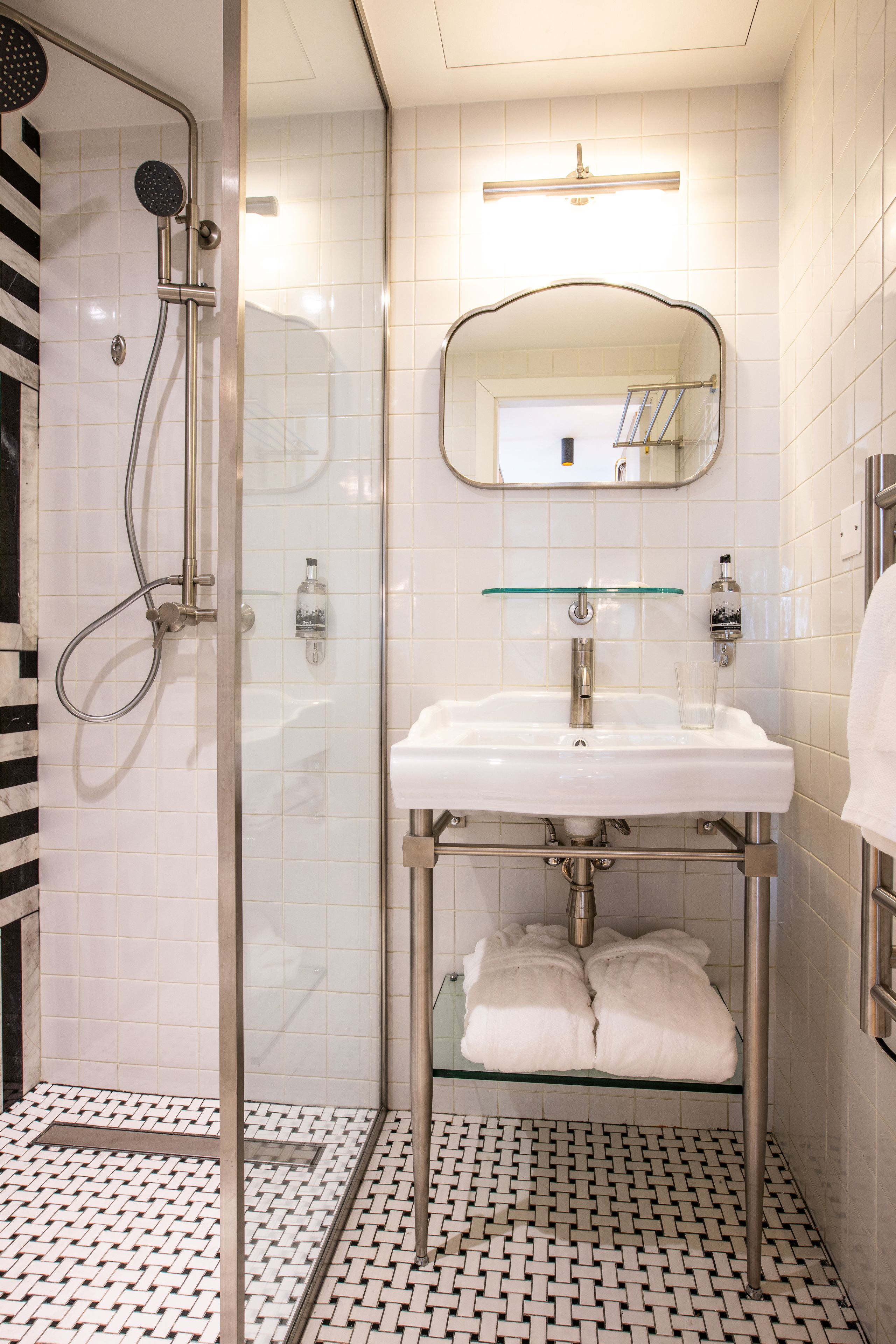A modern bathroom with a glass shower enclosure, a white sink with a glass shelf, and a mirror above the sink.