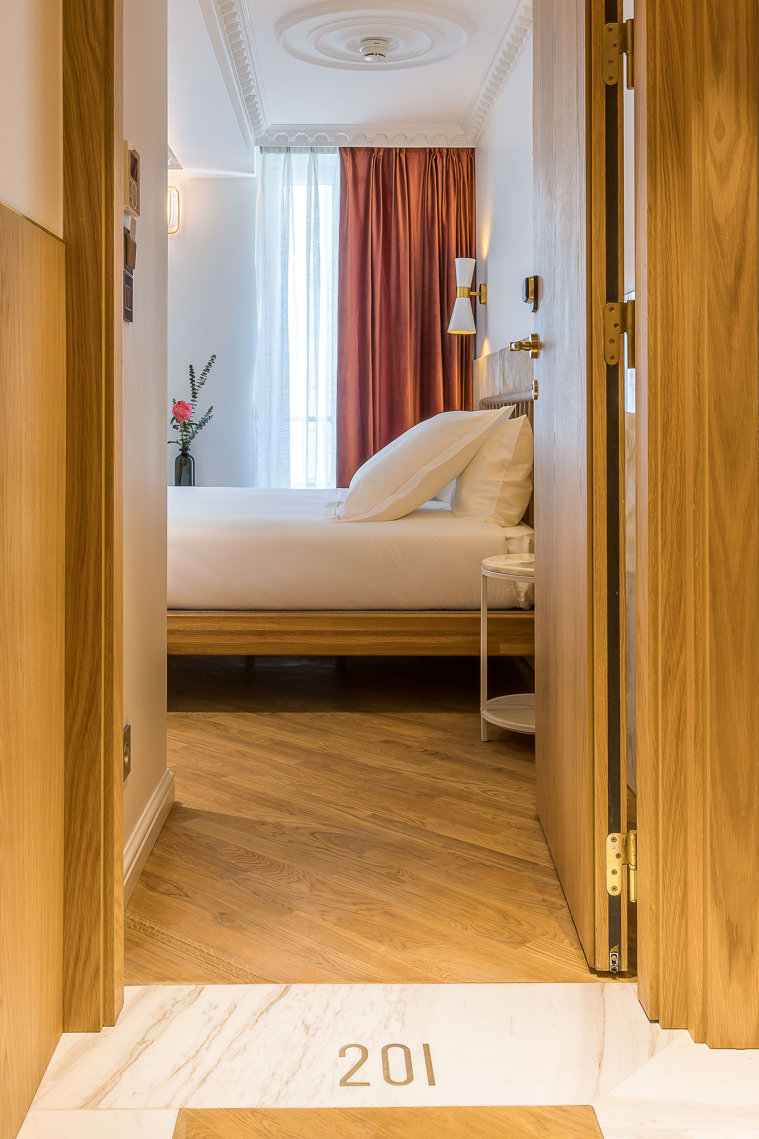 Ein Hotelzimmer mit Bett, Nachttisch, Lampe und einem Fenster mit Vorhängen.
