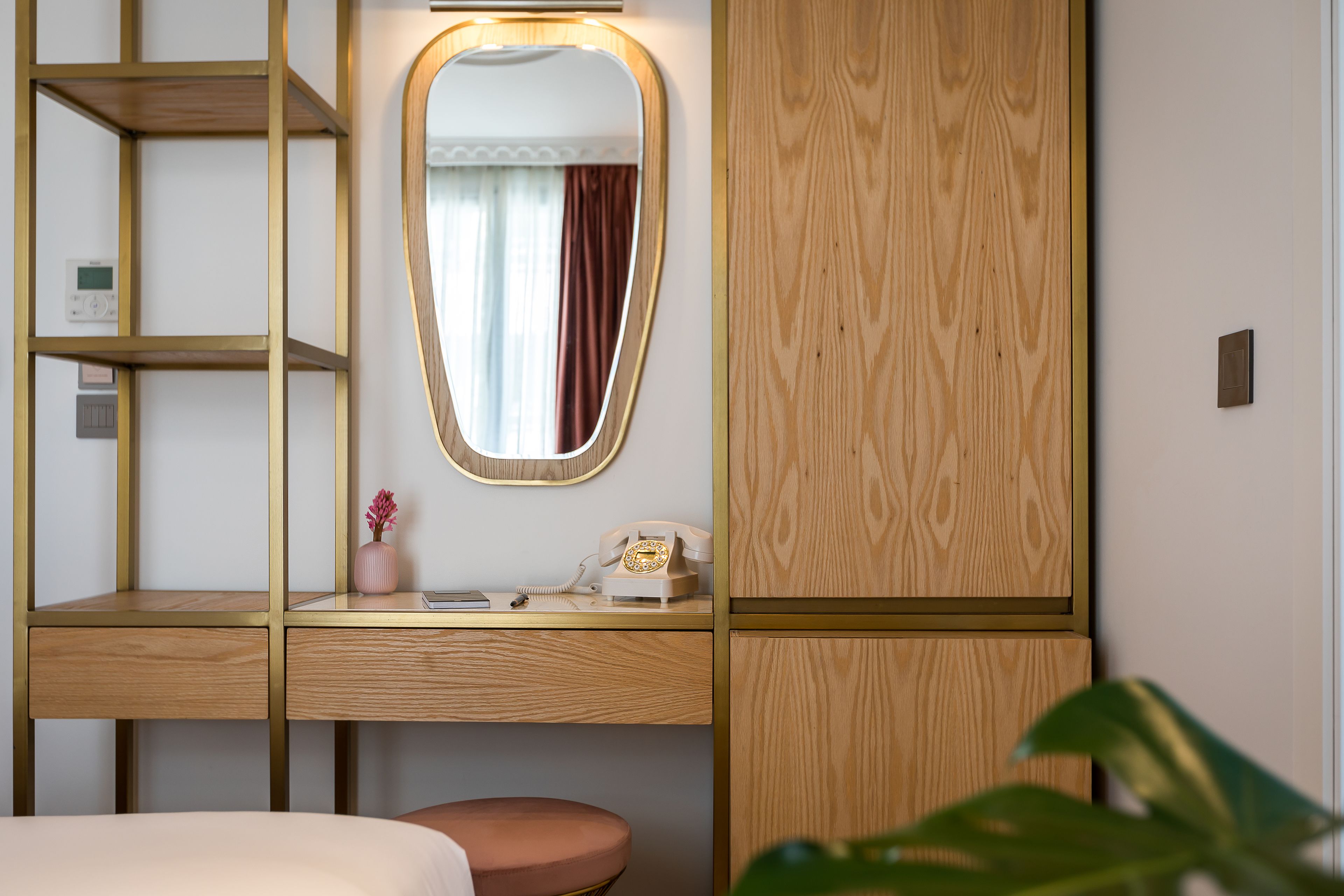 A hotel room with a wooden desk, a mirror, a telephone, and a small plant.