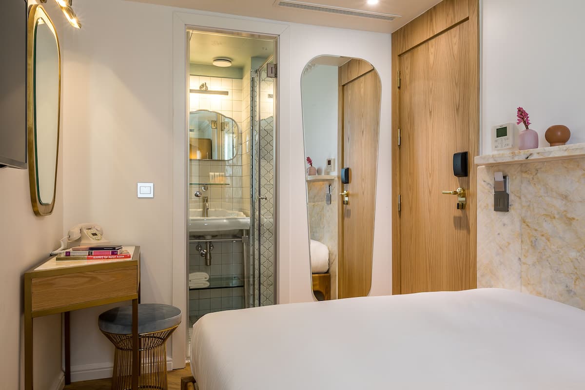 Un dormitorio moderno con una cama grande, una puerta de madera, un baño con ducha de vidrio y un tocador con espejo.