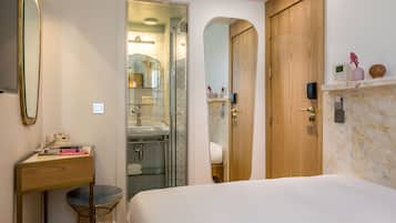 A modern bedroom with a large bed, a wooden door, a bathroom with a glass shower, and a vanity with a mirror.