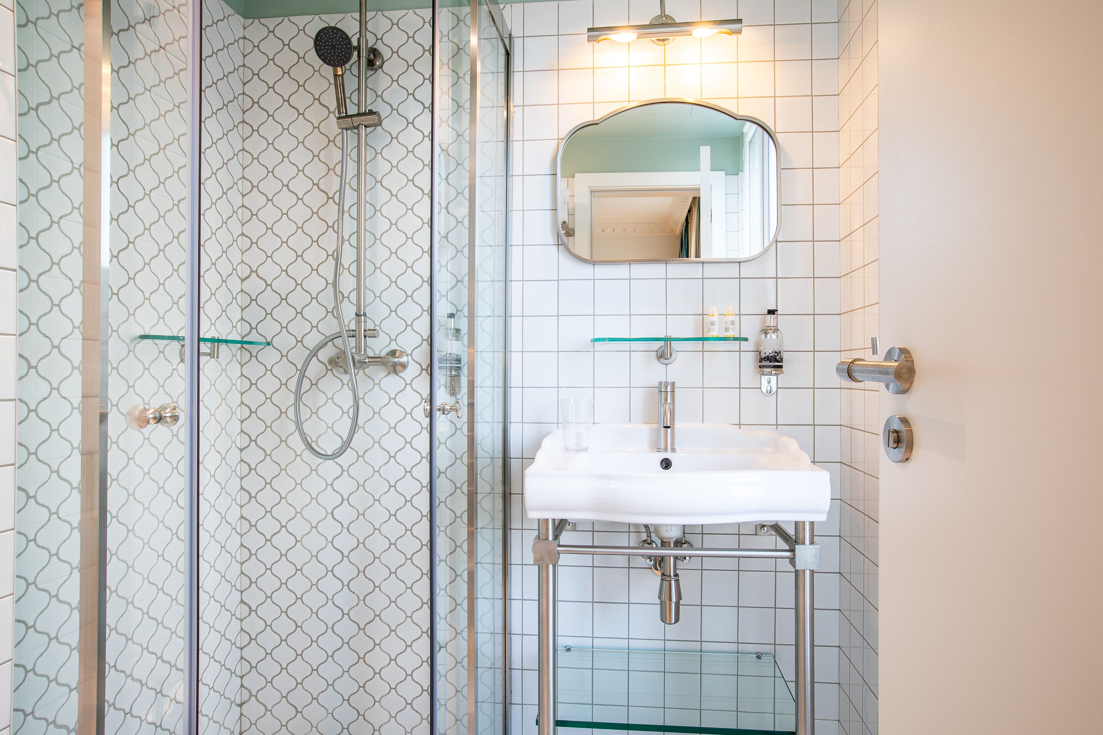 Une salle de bain avec une douche à parois de verre, un lavabo blanc avec un miroir au-dessus et une étagère en verre.