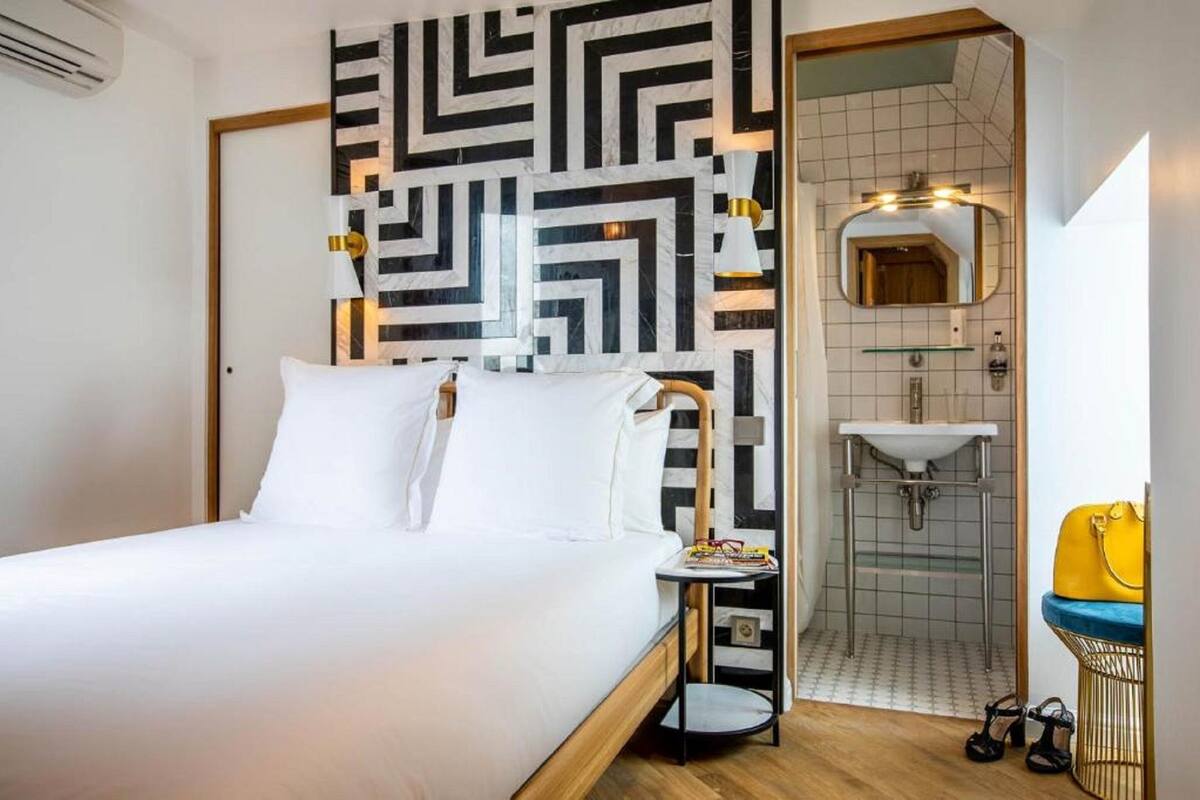 Una habitación de hotel con cama, mesita de noche, espejo, lavabo y ducha.
