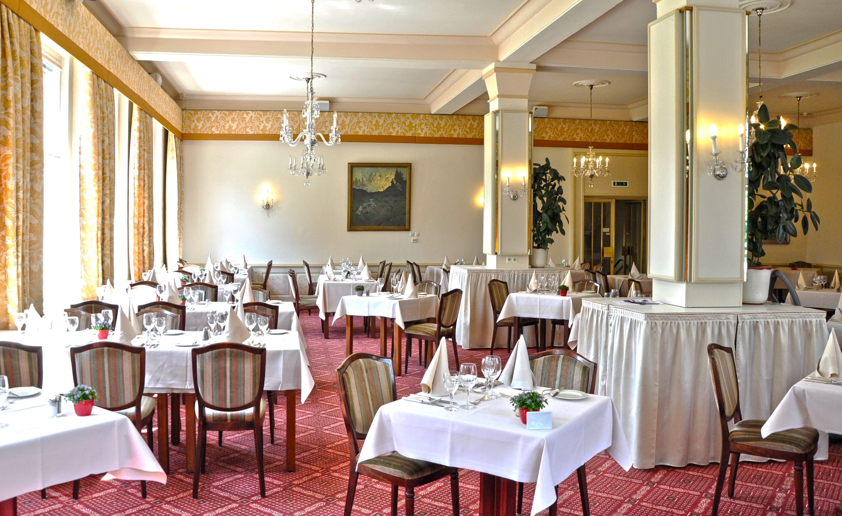 A formal dining room with multiple tables set for service, chairs, and a large chandelier.