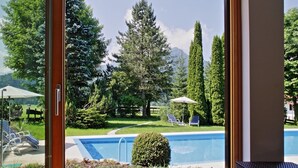 A pool area with lounge chairs and umbrellas, surrounded by trees and a mountain view. - Hotel Wittelsbacher Hof (Oberstdorf)