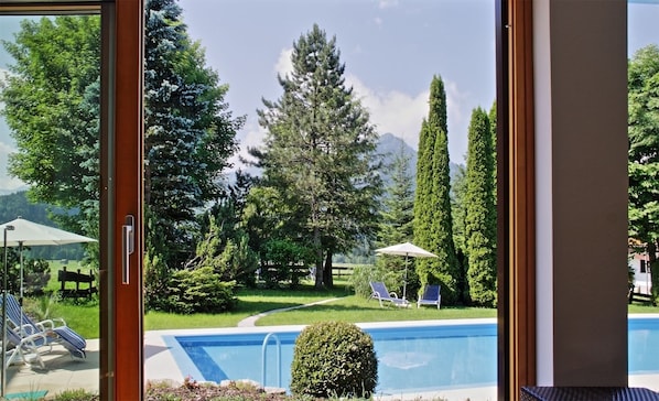 A pool area with lounge chairs and umbrellas, surrounded by trees and a mountain view. - Hotel Wittelsbacher Hof (Oberstdorf)