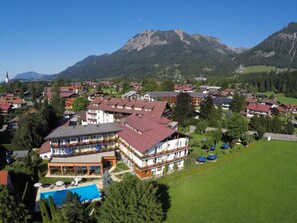 Un hotel con varias plantas, piscina y montañas al fondo.