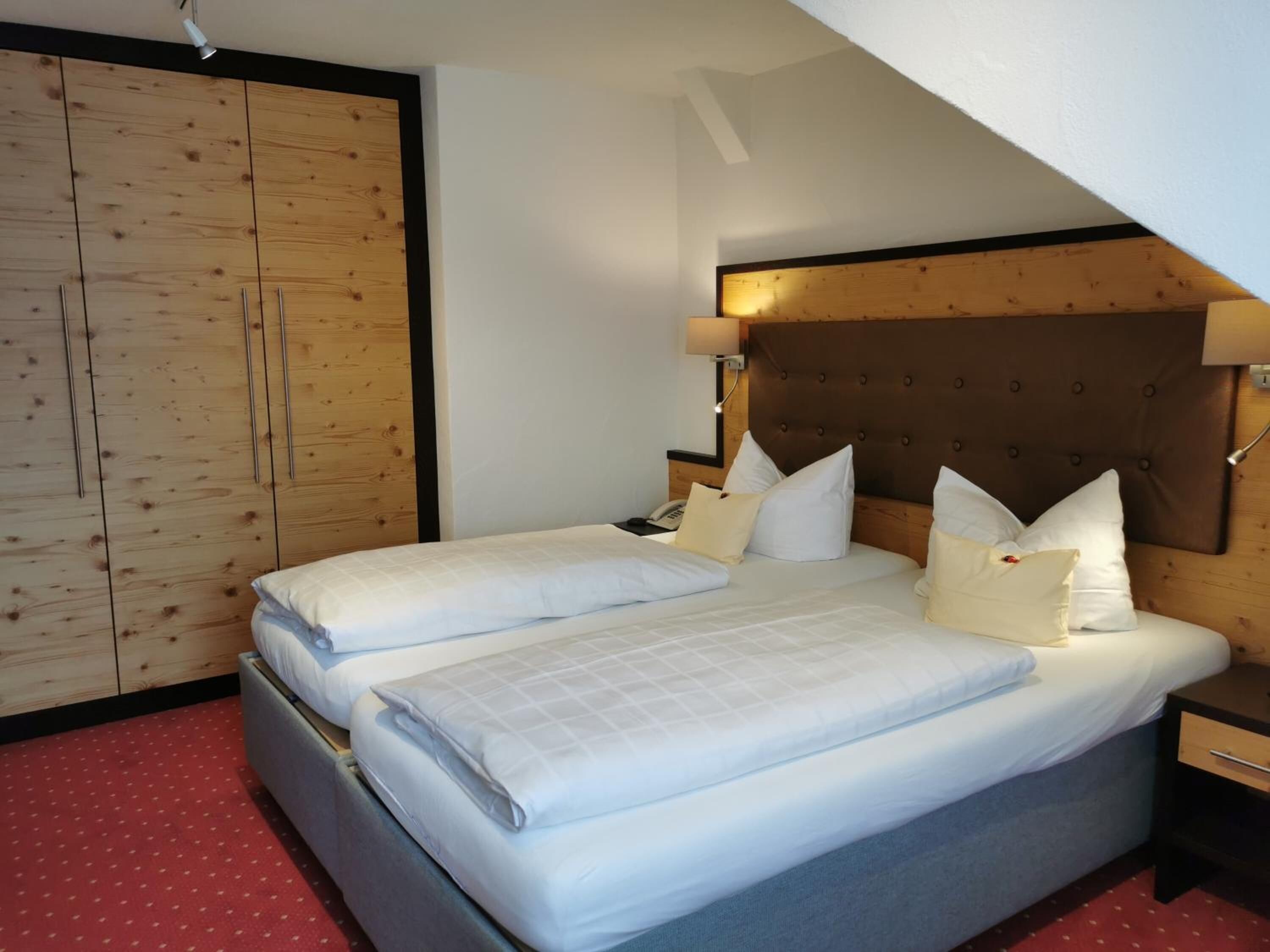 Une chambre avec deux lits, une armoire en bois et un plafond en pente.