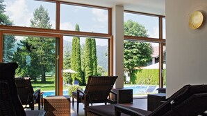 A spacious room with large windows, wicker furniture, and a view of a swimming pool and greenery. - Hotel Wittelsbacher Hof (Oberstdorf)