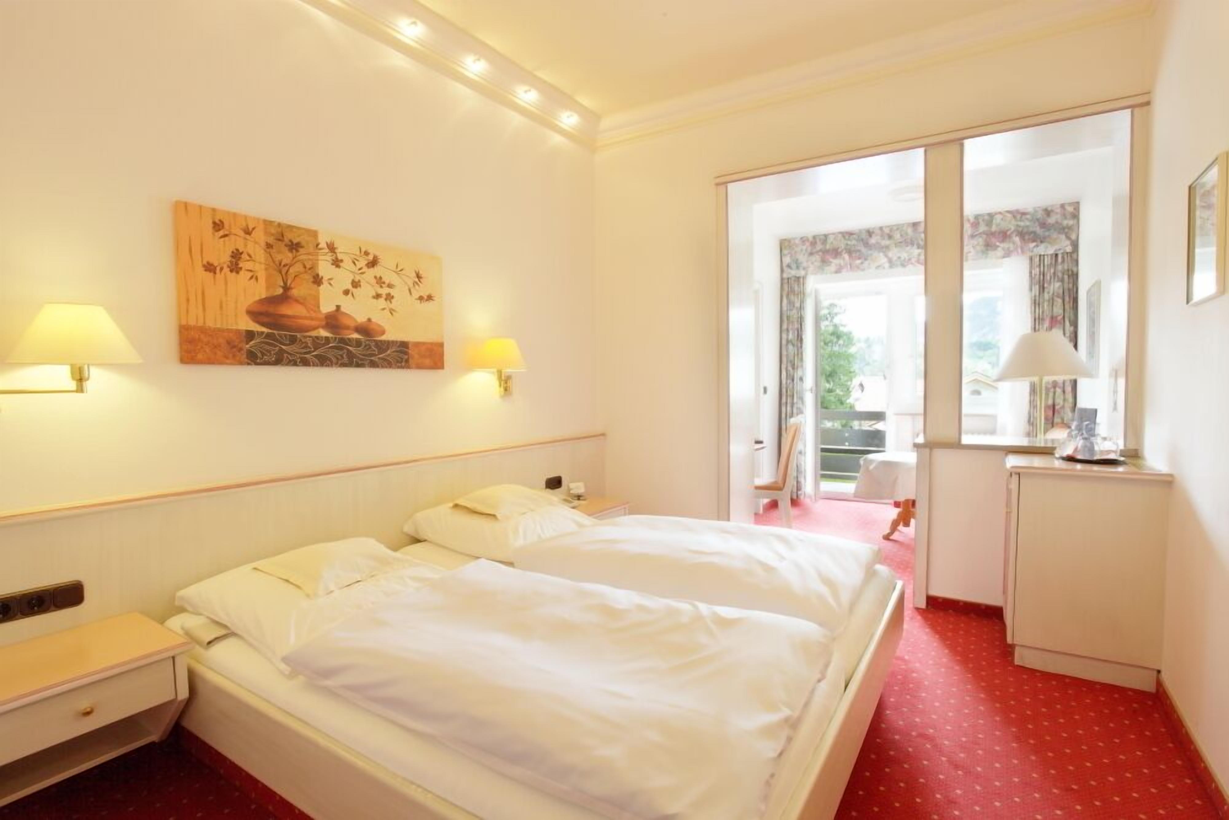 A hotel room with a bed, bedside lamps, a painting, and a window with a view.