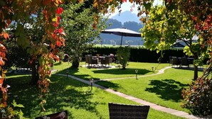 An outdoor seating area with a table and chairs, a sign with the number 82, and a view of a grassy lawn and distant mountains. - Hotel Wittelsbacher Hof (Oberstdorf)