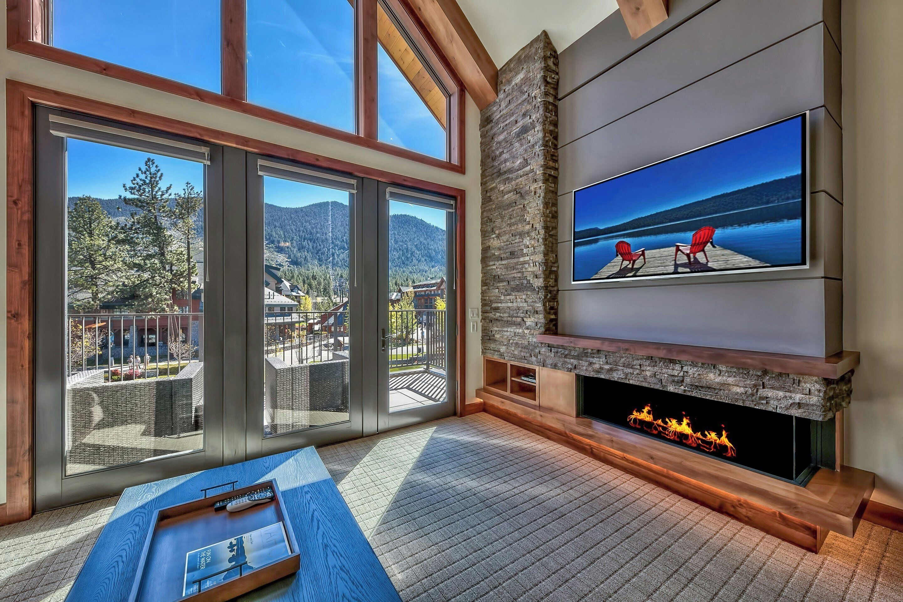 Una sala de estar moderna con chimenea, televisor grande y vista a un lago a través de ventanales.