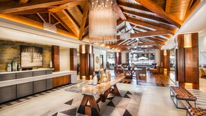 A spacious lobby with a high ceiling, wooden beams, a central table, and seating areas.