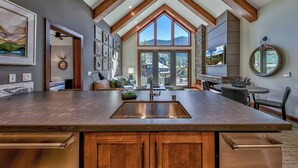 A modern kitchen with a large island, wooden beams, and a view of mountains through large windows.