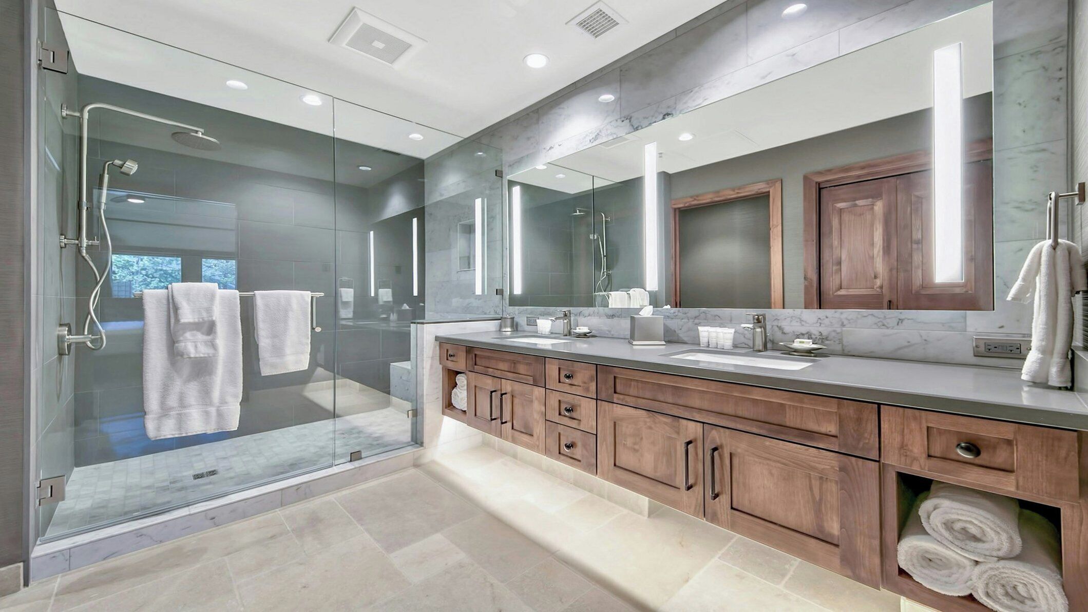 Un baño moderno con ducha envuelta en vidrio, un espejo grande y armarios de madera.