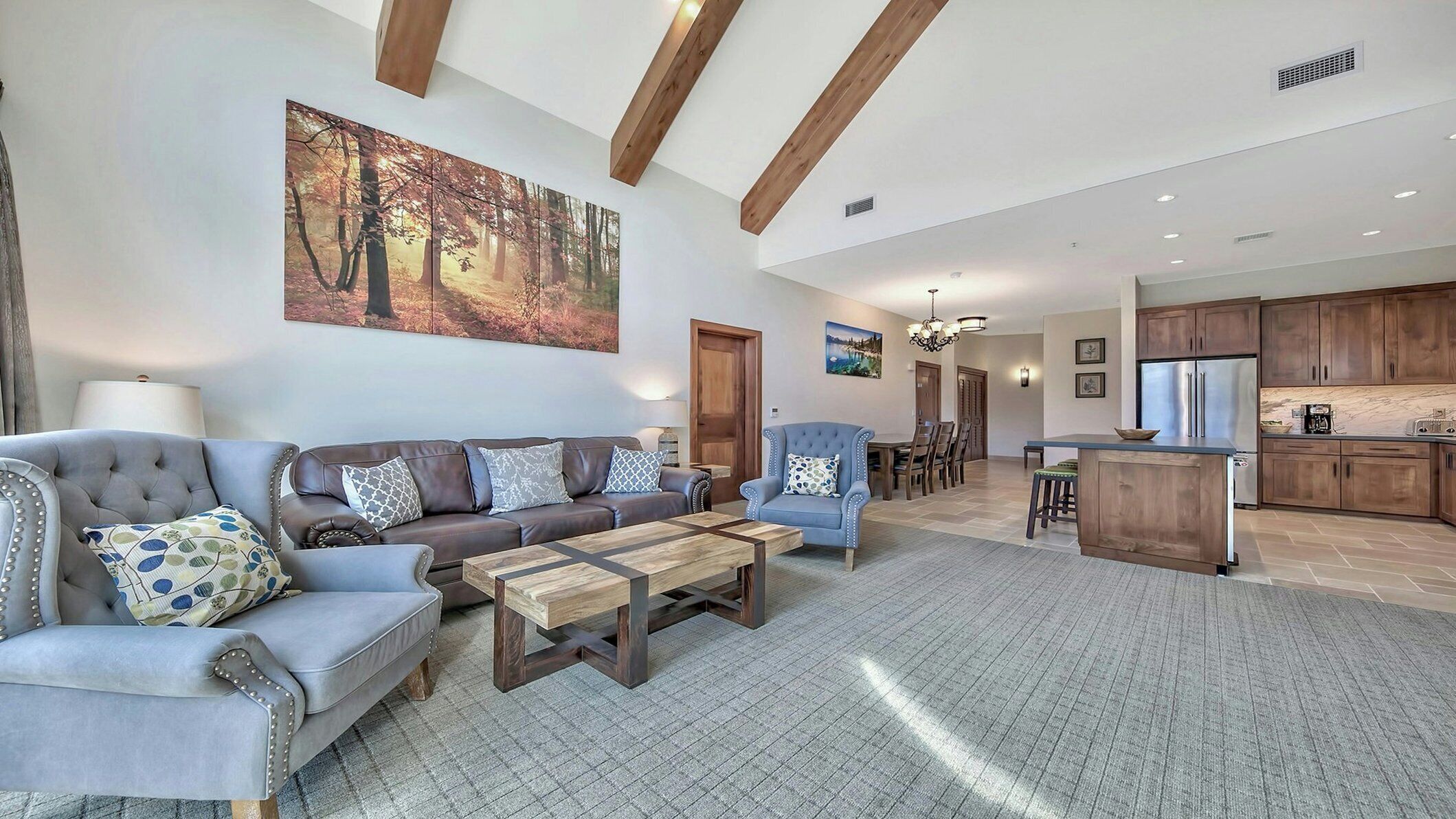 A spacious living room with a sofa, armchairs, and a coffee table. A dining area with a table and chairs is visible in the background.