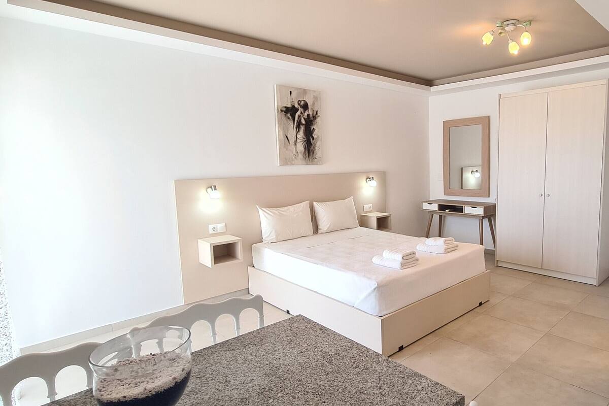 Een slaapkamer met een bed, nachtkastjes, een dressoir, een spiegel en een schilderij aan de muur.