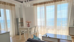 A modern living room with a sofa, a dining table with chairs, and a kitchen area with a refrigerator.