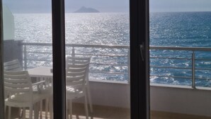 A balcony with a view of the sea and a distant island. There are white plastic chairs and a table on the balcony.