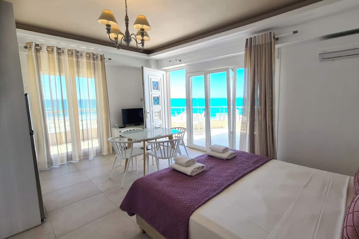 Een hotelkamer met een bed, een bureau, een stoel en een televisie. Er is een balkon met uitzicht op de oceaan.