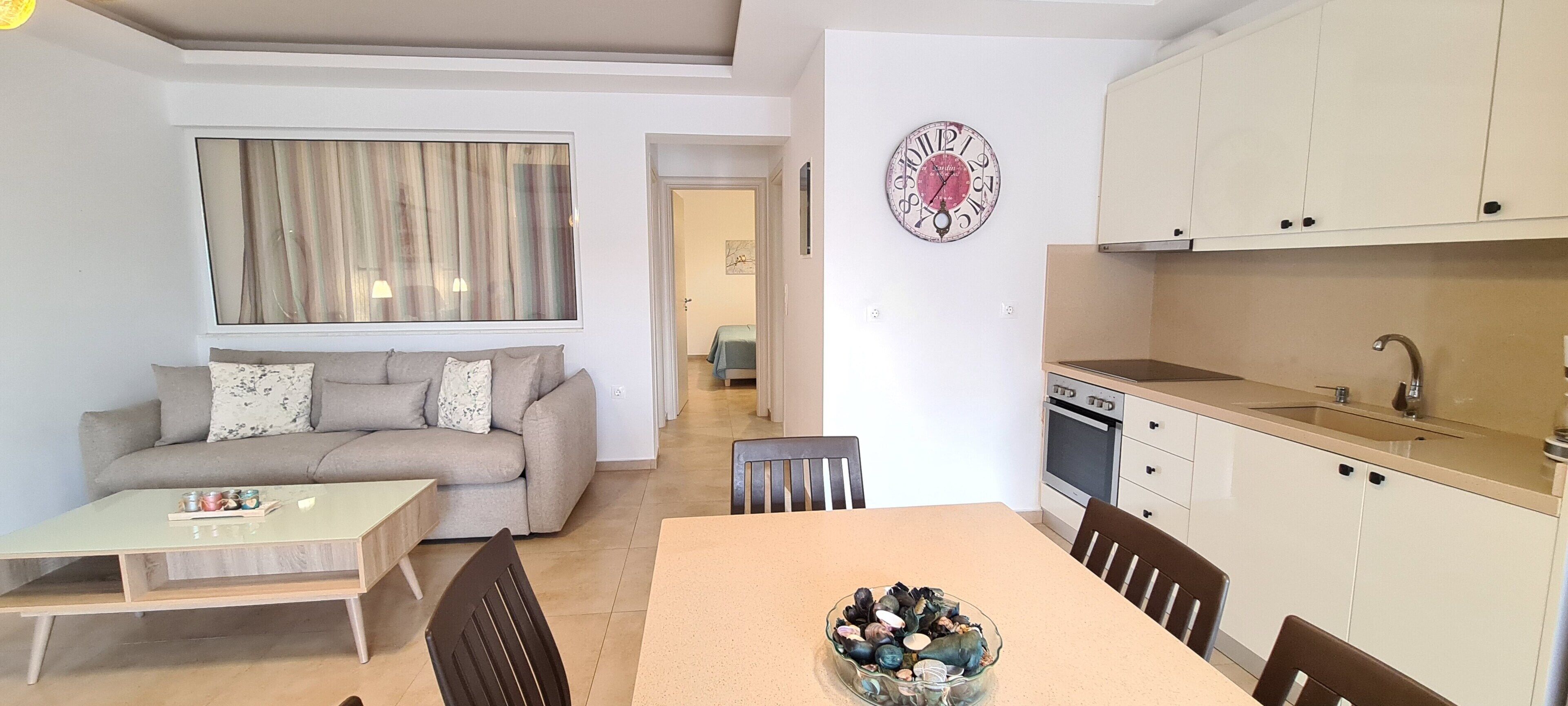 A modern apartment with a dining area, kitchen, and a living room with a sofa and a painting.