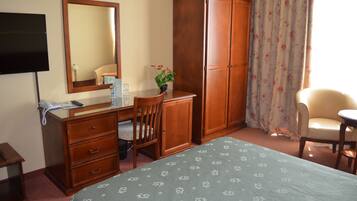 A hotel room with a bed, a desk with a chair, a wardrobe, a television, and a window with curtains.